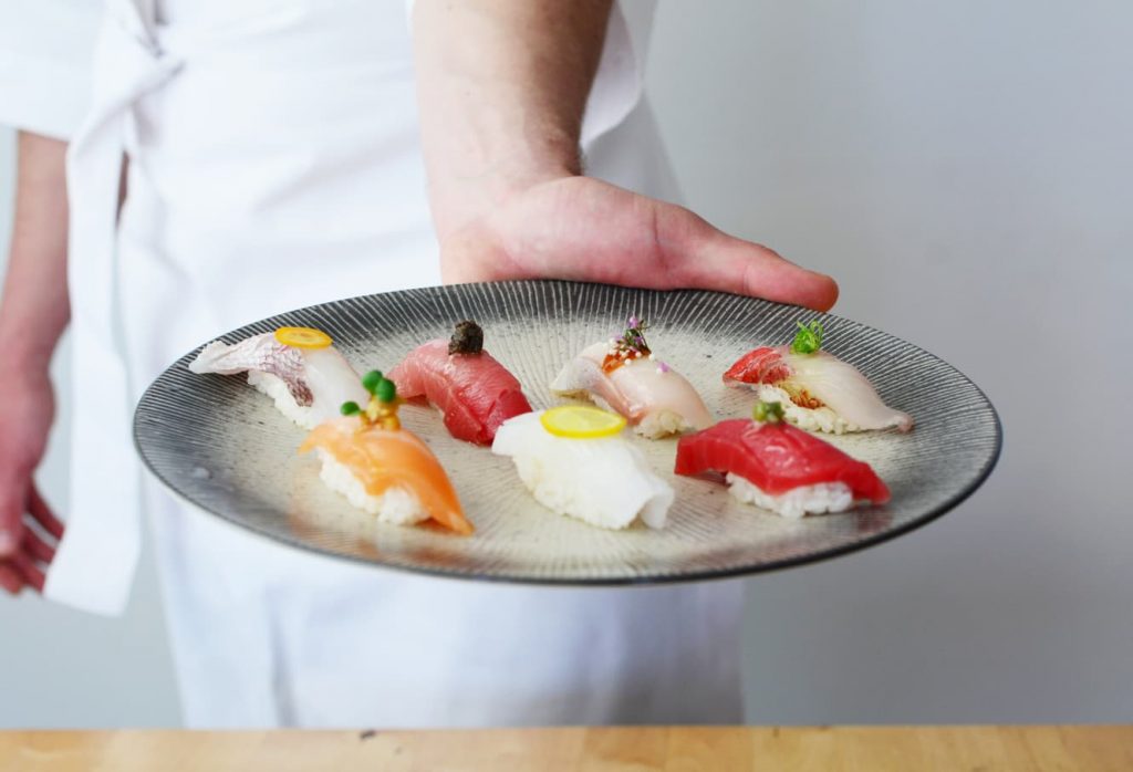 sushi chef presents plate with nigiri selection