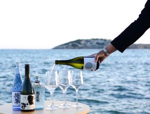 sommelier is pouring sake into the glass, Ibiza's seashore in the background